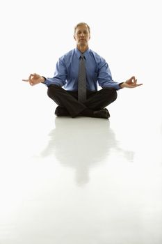 Caucasian middle aged businessman meditating in yoga lotus pose on floor.