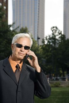 Caucasian middle aged businessman in sunglasses holding cell phone outdoors.