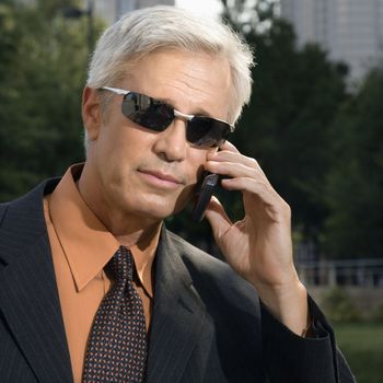 Caucasian middle aged businessman in sunglasses talking outdoors on cell phone.