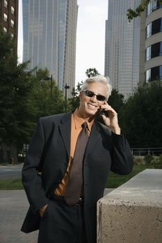 Caucasian middle aged businessman in sunglasses talking outdoors on cell phone.