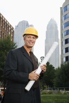 Caucasian middle aged businessman holding blueprints wearing hard hat.