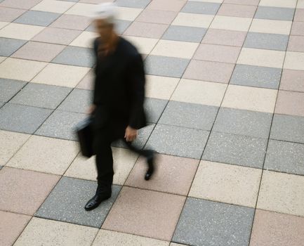 Motion blur of Caucasian businessman walking outdoors with briefcase.