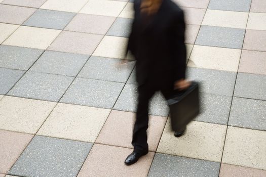 Motion blur of Caucasian businessman walking outdoors with briefcase.