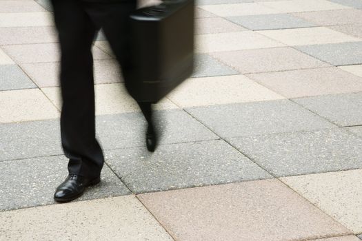 Motion blur of businessman legs walking outdoors with briefcase.