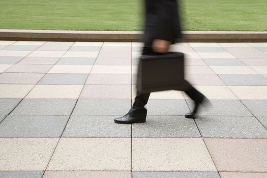 Motion blur of businessman legs walking outdoors with briefcase.