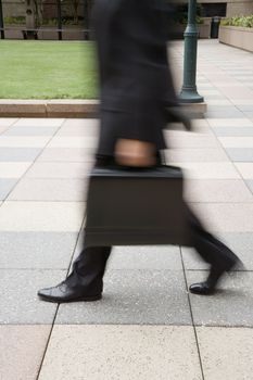 Motion blur of Caucasian businessman walking outdoors with briefcase.