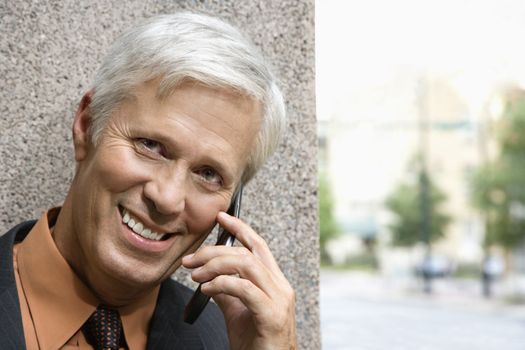 Caucasian middle aged businessman talking on cell phone smiling at viewer.