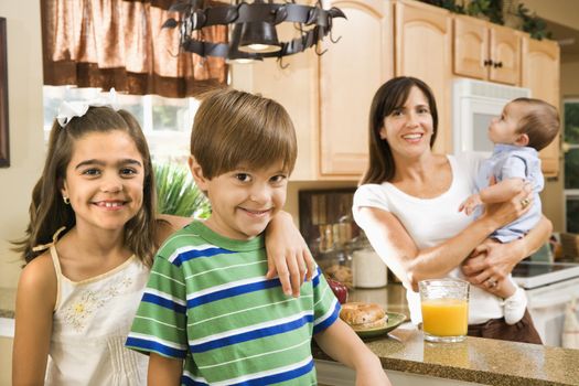 Hispanic mother and children smiling at viewer in kitchen.