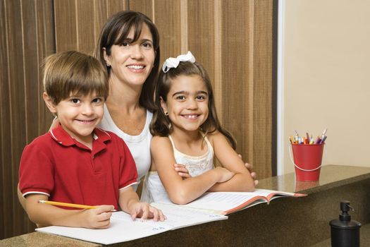 Hispanic mother and children smiling at viewer with homework.