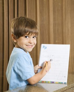 Hispanic boy holding up homework and smiling at viewer.
