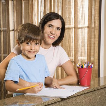 Hispanic mother and son with homework smiling at viewer.