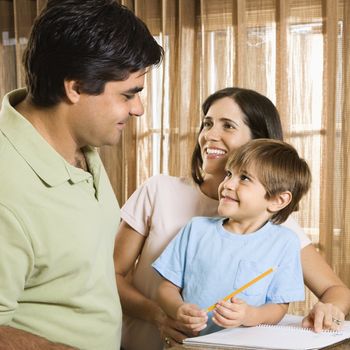 Hispanic parents making eye contact with son doing homework.