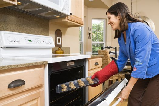 Side view of Hispanic mid adult woman putting cookies into oven.