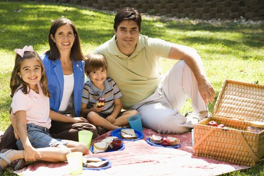 Hispanic family picnicking in the park and smiling at viewer.