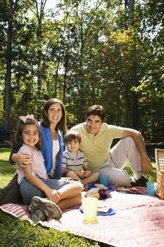 Hispanic family picnicking in the park and smiling at viewer.