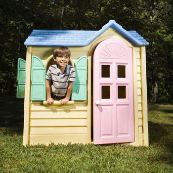 Hispanic boy in window of outdoor playhouse smiling at viewer.