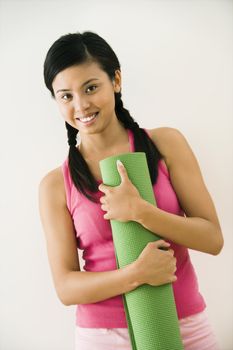 Portrait of smiling young Asian woman holding exercise mat.