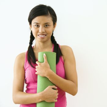 Portrait of smiling young Asian woman holding exercise mat.