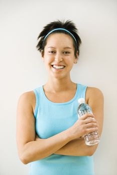 Young woman in exercise clothes holding bottle of water smiling.