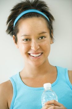 Head and shoulder portrait of young woman in fitness wear holding bottled water and smiling.