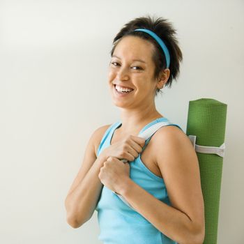 Young woman holding yoga mat and smiling.