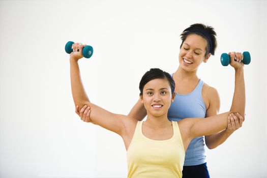 Young woman lifting hand weights while another woman helps position her arms.