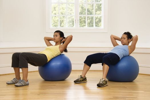 Two young women doing ab workout on balance balls.