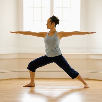 Young woman doing yoga warrior pose indoors by sunlit window.