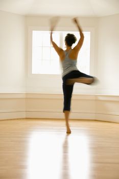 Young woman in motion jumping and dancing indoors by sunlit window.