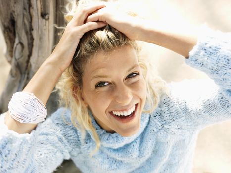 Portrait of pretty young blond woman sitting on beach in Maui, Hawaii smiling and holding back hair with hands.