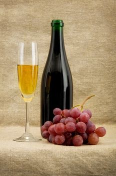 Champagne bottle, goblet, grapes on sacking
