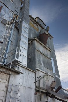 industrial background - a metal exterior of old grain elevator with pipes, ducts, ladders and chutes against sky