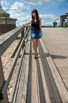 Young, sexy  woman in short skirt goes for a walk on the old-time bridge.
