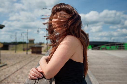 Portrait of young, beautiful woman with wind waving her hair standing on the old-time bridge.