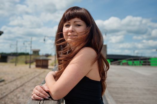 Portrait of young, beautiful woman with wind waving her hair standing on the old-time bridge.