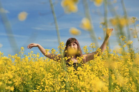 Young happy woman on summer day in the flower meadow and blue sky at the background.
