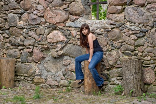 Young beautiful woman sitting on the log near old castle ruins.
