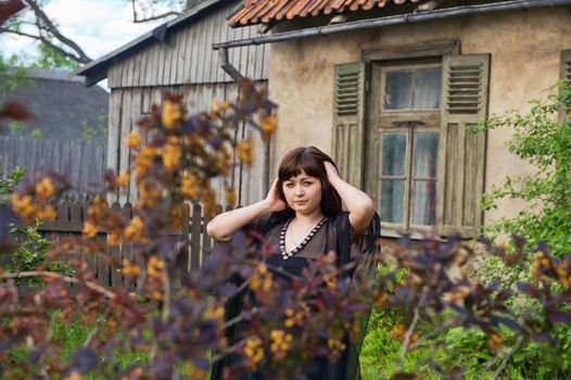 Young beautiful woman stand in the garden nearby old house.
