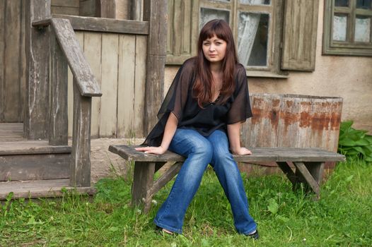 Young beautiful woman sit on the bench in front of old house.
