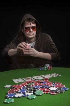 Man with sun glasses playing poker on green table. Chips and cards on the table.