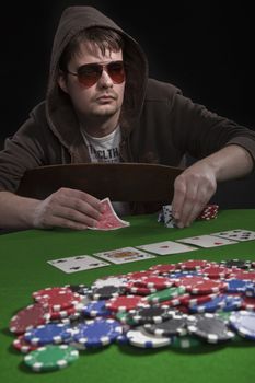 Man with sun glasses playing poker on green table. Chips and cards on the table.