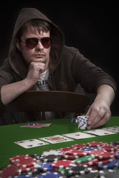 Man with sun glasses playing poker on green table. Chips and cards on the table.