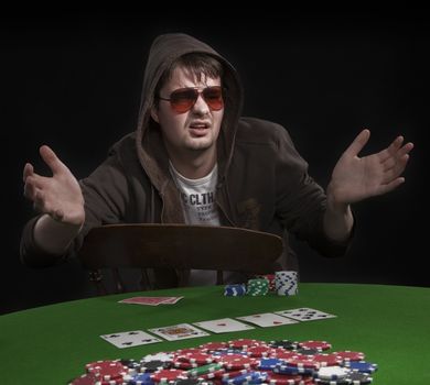 Man with sun glasses playing poker on green table. Chips and cards on the table.