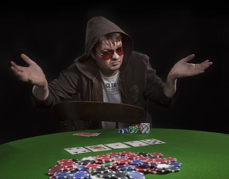 Man with sun glasses playing poker on green table. Chips and cards on the table.