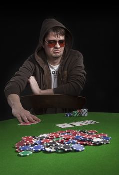 Man with sun glasses playing poker on green table. Chips and cards on the table.