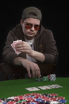 Man with sun glasses playing poker on green table. Chips and cards on the table.