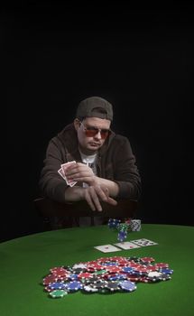 Man with sun glasses playing poker on green table. Chips and cards on the table.