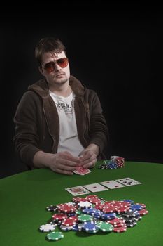 Man with sun glasses playing poker on green table. Chips and cards on the table.