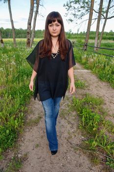 Young beautiful woman on the walk on the road in the middle of dandelion meadow.
