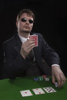 Man in suit with sun glasses playing poker on green table. Chips and cards on the table.